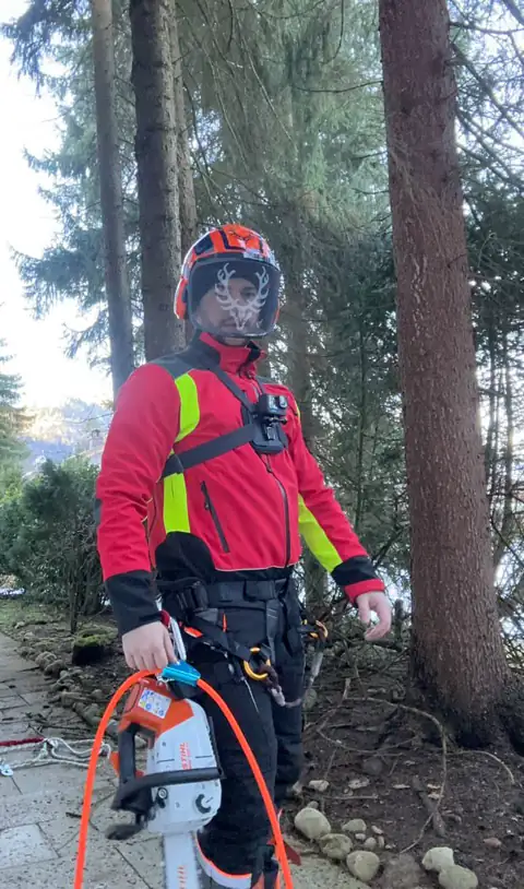 Baumkletterer in Schutzausrüstung mit vorbereitetem Motorsägen-Equipment am Einsatzort